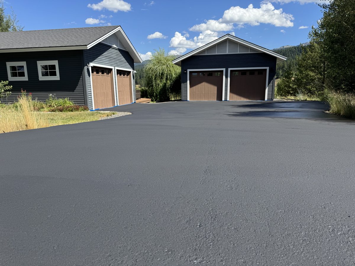 Freshly sealcoated driveway at a mountain home, garage doors masked with tape during the job